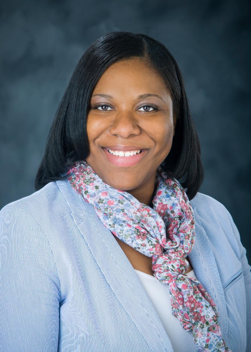women in blue top and pink scarf smiling at the camera in a portrait style headshot